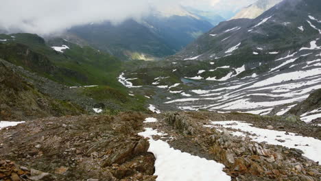 Rocky-mountain-terrain-of-valley-in-Zernez-Switzerland-during-summer-day-as-snow-melts,-aerial