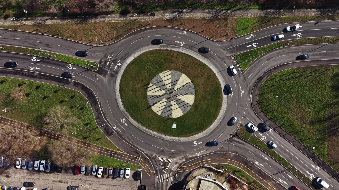 Traffic circle is surrounded by roads and grass with multiple vehicles and clear markings visible on the ground during daylight hours