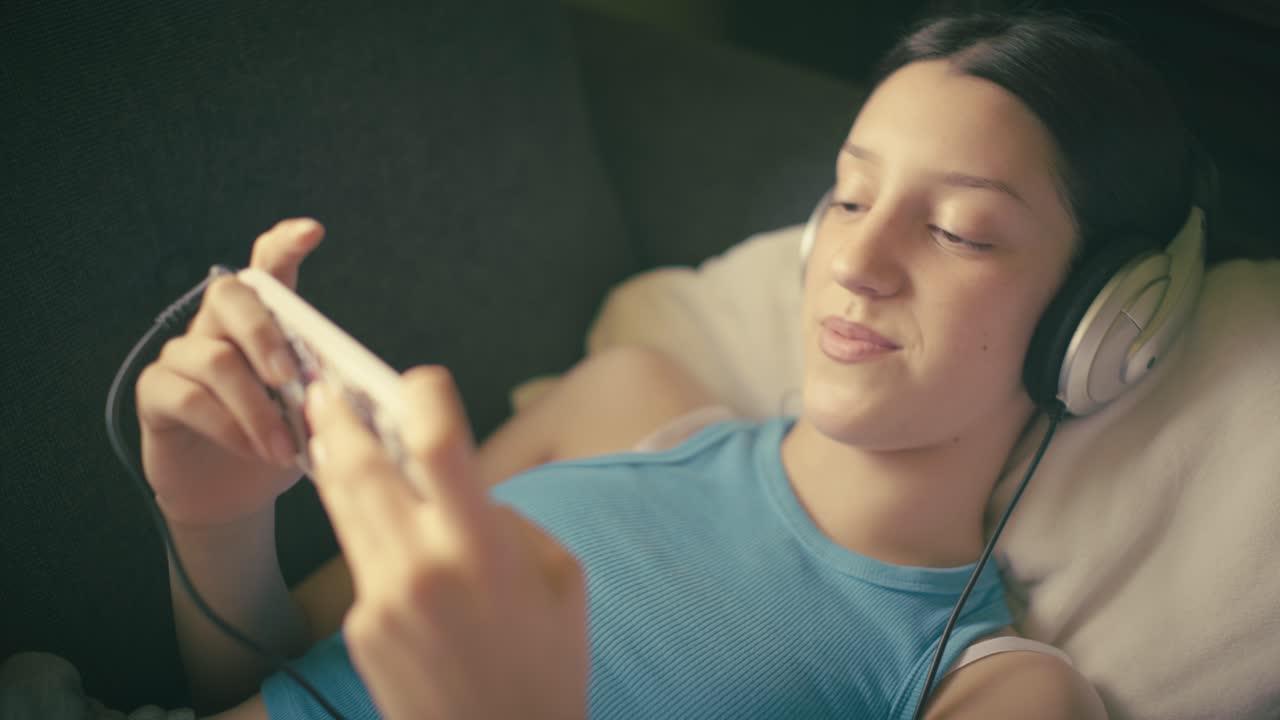 Teen girl relaxing at home, listening to music with headphones and using her smartphone. A calm, intimate moment of digital leisure in a cozy setting.