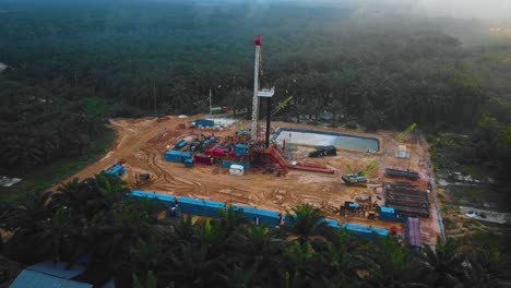 Cinematic-Drone-Shot-of-Onshore-Drilling-and-Workover-Rig-structure-and-Rig-equipment-for-oil-exploration-and-exploitation-in-the-middle-of-jungle-surrounded-by-palm-oil-trees-during-sunset-time