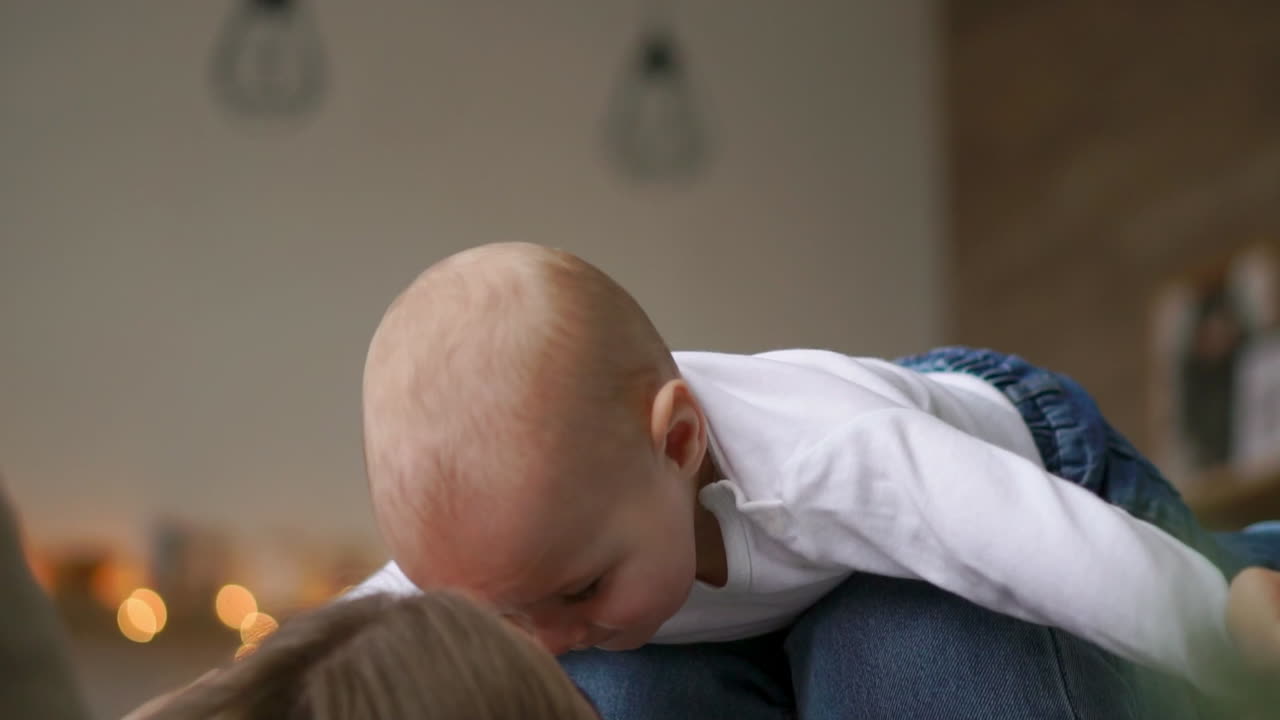 엄마는 침대에 누워 있는  ⁇   ⁇ 크 트립을 입은 아기와 함께 놀고, 아기가 날아다니고 웃고 있습니다. 엄마와 아이가 함께 놀고 있는 타임  ⁇ 스. 비행 시 ⁇ 레이션