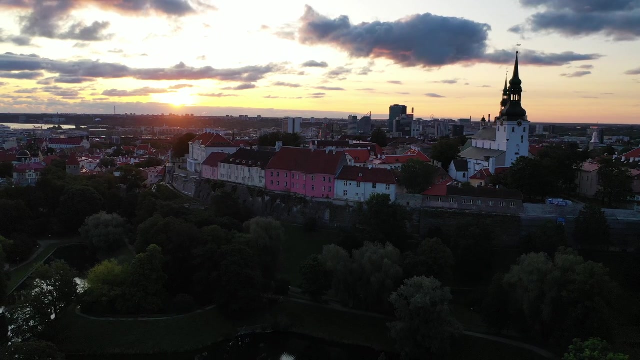 Filmato mozzafiato con drone del Centro Storico medievale di Tallinn al tramonto. L'inquadratura mostra la Collina di Toompea, la Cattedrale di Santa Maria e gli edifici dai tetti rossi sotto un cielo drammatico di nuvole rosa e arancioni.