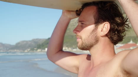 young man carrying surfboard on head at beach