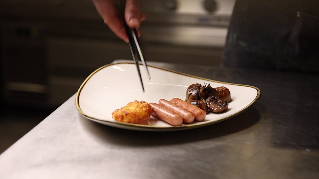 Chef Plating Hash Brown, Sausages, and Mushrooms in a Commercial Kitchen