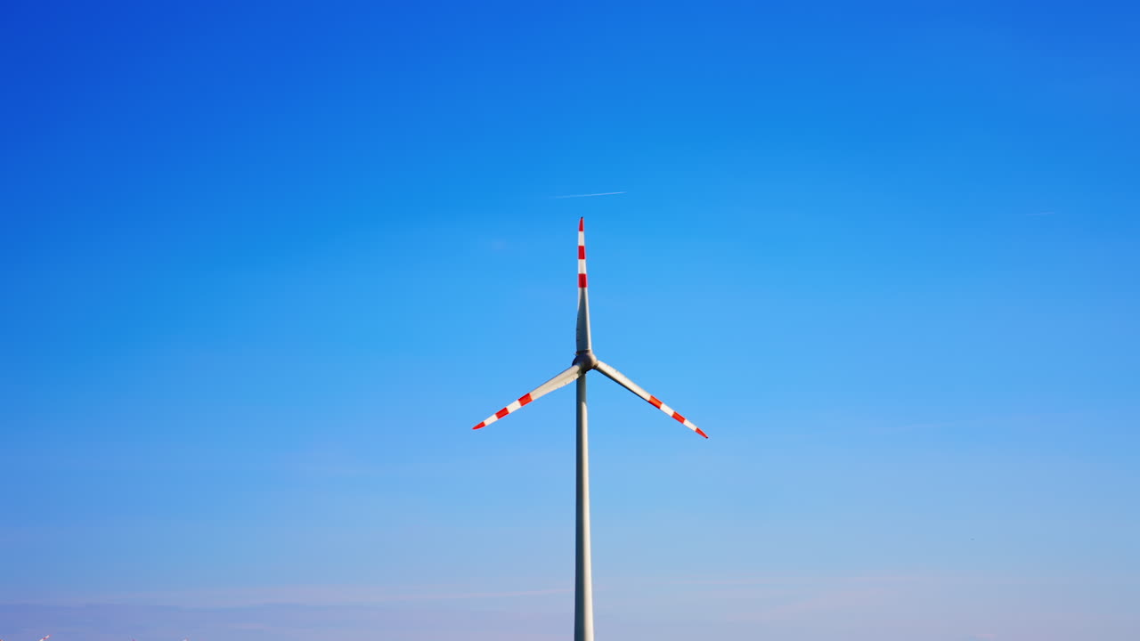 White and red stripes on the rotating blades of the wind mill. Clear blue sky at backdrop