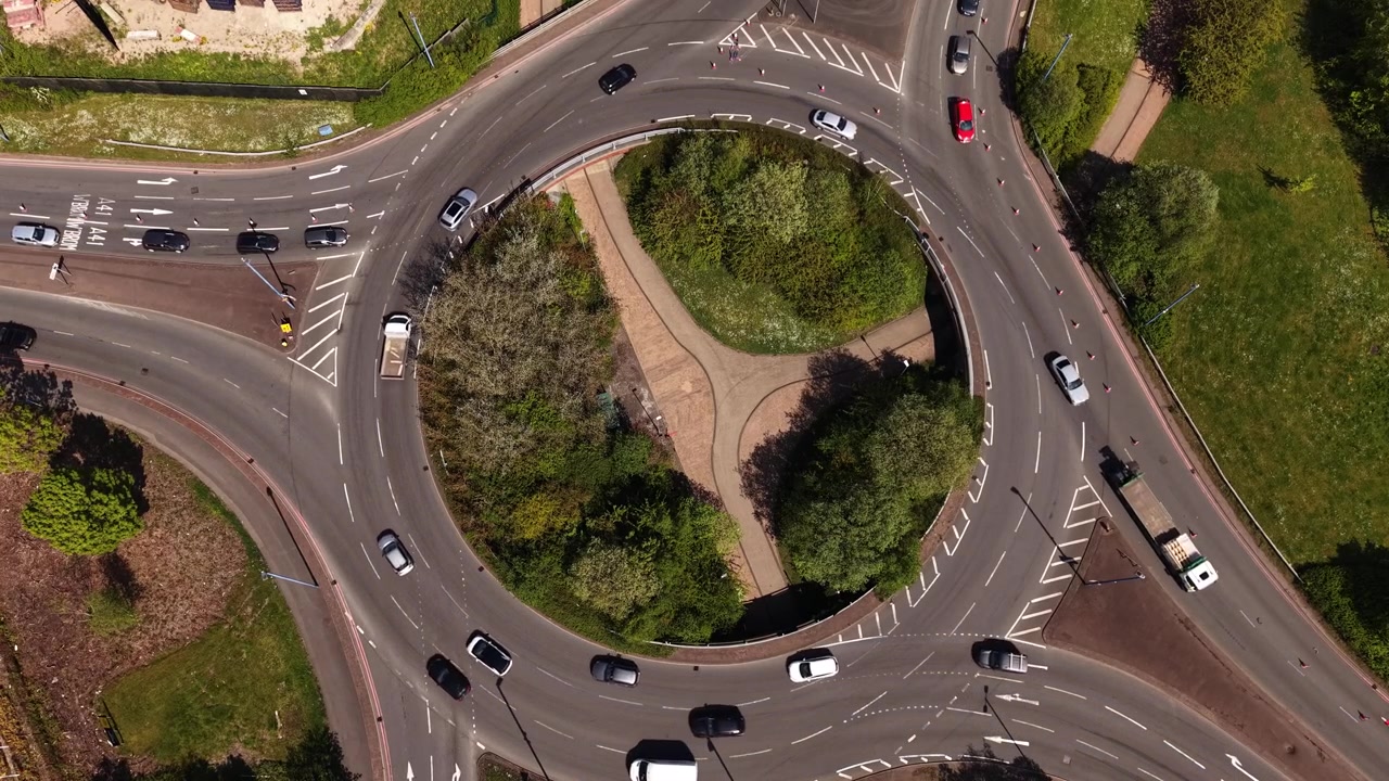Drone top down footage of cars, vans and trucks driving around a busy roundabout in England. Urban traffic flow and modern road infrastructure aerial scene.