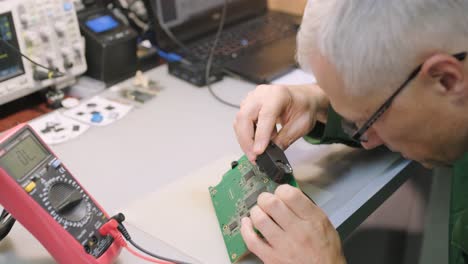 electronic equipment repair shop. the engineer technician solders the printed circuit board of an electronic device under a microscope.