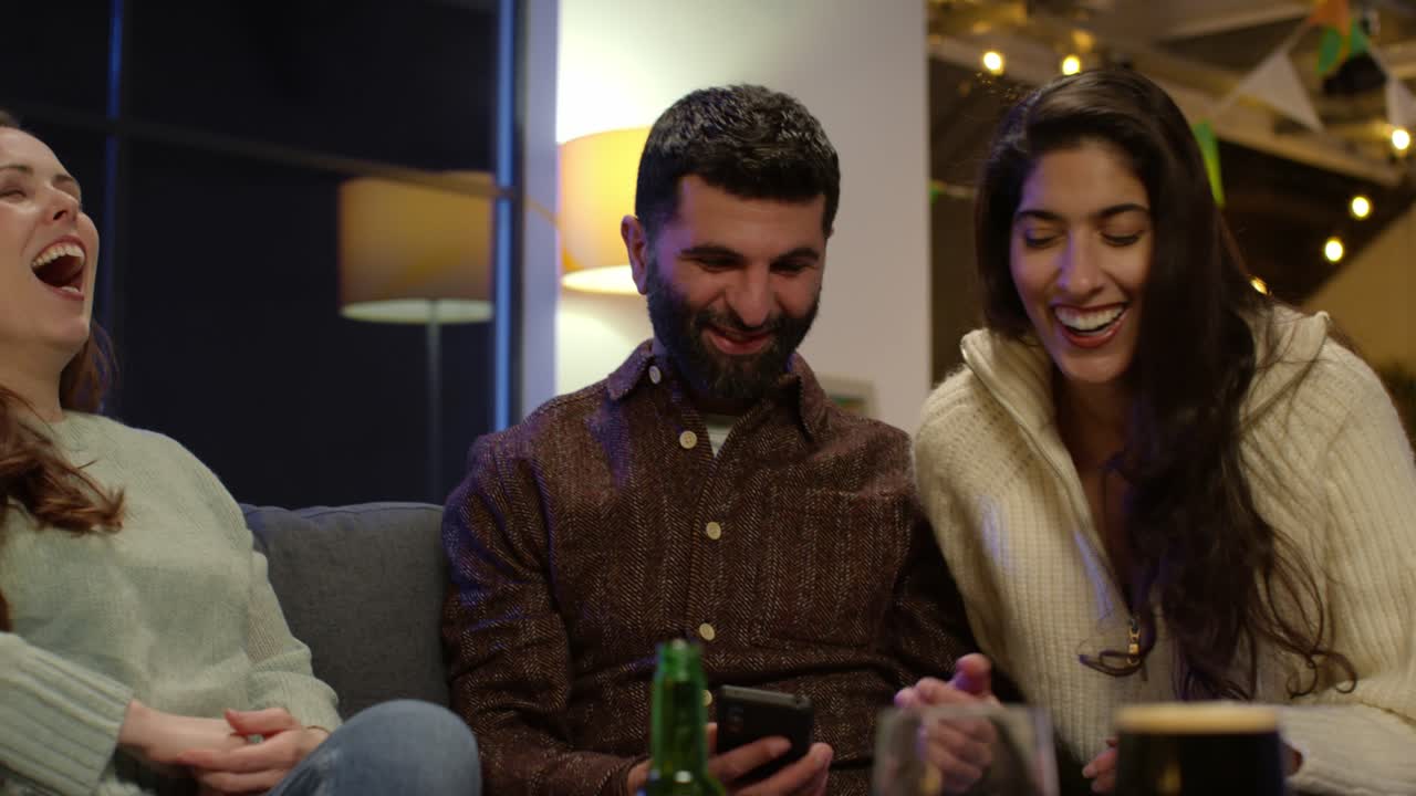 Gruppo di amici che si traveste a casa o in un bar, festeggiando a una festa di San Patrizio e in posa per un selfie al telefono 1