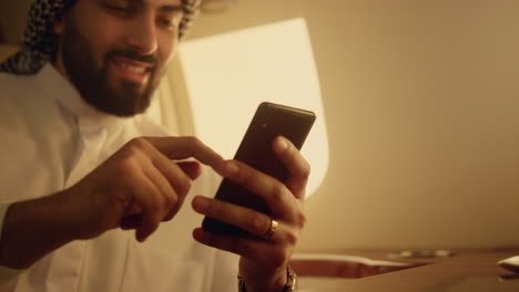 smiling arabian using smartphone closeup. cheerful man swiping phone in hands