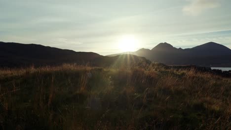 Un-ángulo-De-Cámara-Lento-Hacia-La-Derecha-Mientras-El-Sol-Se-Pone-Detrás-De-Las-Montañas-En-El-Fondo,-Proyectando-Una-Luz-Dorada-Sobre-Los-Pastizales-Nativos-En-Primer-Plano