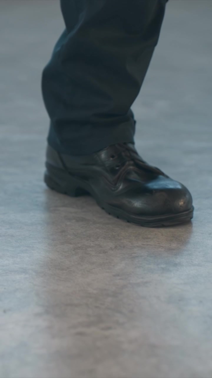 Close up of feet in black shoes and dark pants walking steadily. Legs move forward with consistent step pattern left shoe leading. Indoor setting focused tightly on lower legs