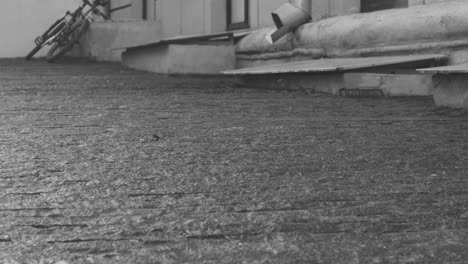 black and white view of a man in coat picking guitar from a case on the floor outdoors