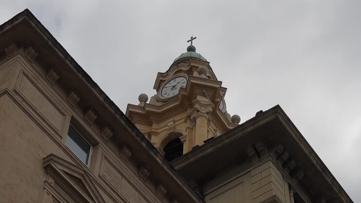 Clipe em panorâmica olhando para cima para a torre abobadada de uma igreja com mostrador de relógio ornamentado e beirais decorativos do telhado