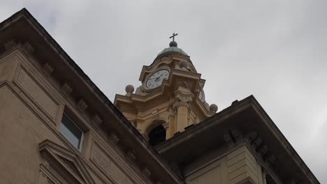 Panning-clip-looking-upwards-at-domed-tower-of-church-with-ornate-clockface-and-decorative-eaves-of-roof