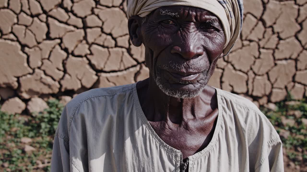 빛으로 은 풍경 속에 서 있는 은 농부, 건조한 아프리카 시골의 거친 환경에 대한 지속적인 탄력성을 드러내는 깊은 줄무 얼굴과 전통 의상을 통해