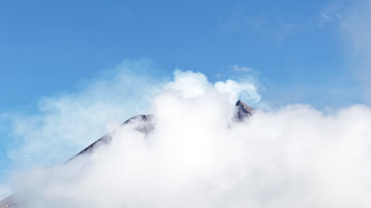 Un filmato aereo 4K mostra la cima del Monte Merapi a Yogyakarta, coperta da fitte nuvole, con un cielo azzurro limpido