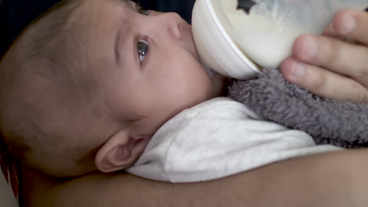 niño indio de 2 meses tratando de beber leche del biberón e inquieto