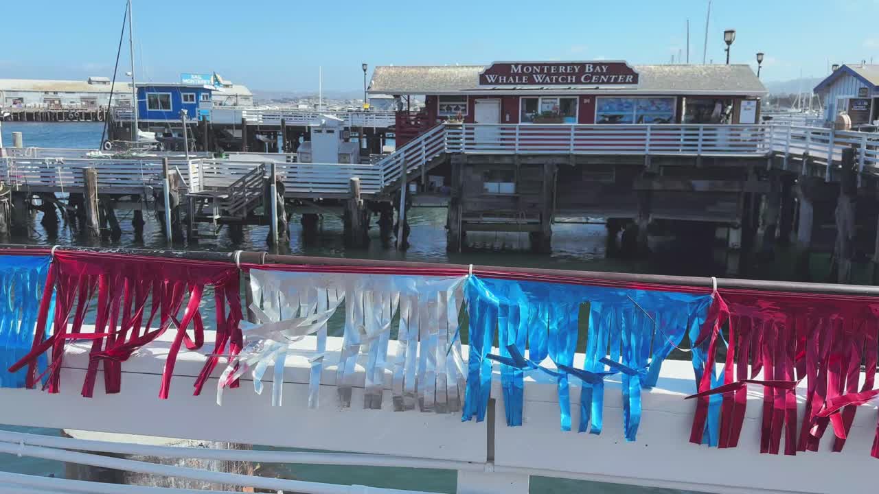 Colourful flags on wooden fence on the pier of Monterey's Fisherman's Wharf and whale watch centre with ocean bay waters