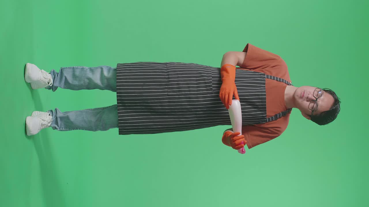 손에 스프레이를 쳐다보고 그린 스크린 스튜디오에서 카메라에 엄지손가락을 아래로 표시하는 아시아 남성 집무원.