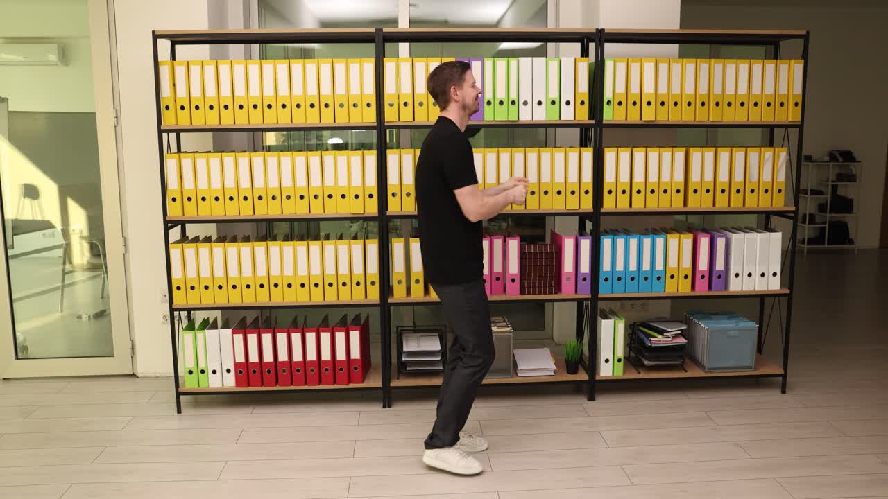 Kancelářský muž tančí u regálů s různými kancelářskými složkami