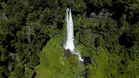 aerial dolly out of salto el leon waterfall streaming on natural pool surrounded by green dense forest, near pucon, chile