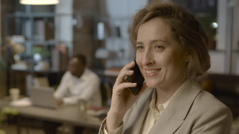 Portrait-Of-A-Smiling-Businesswoman-Talking-On-Mobile-Phone-While-Standing-In-The-Office