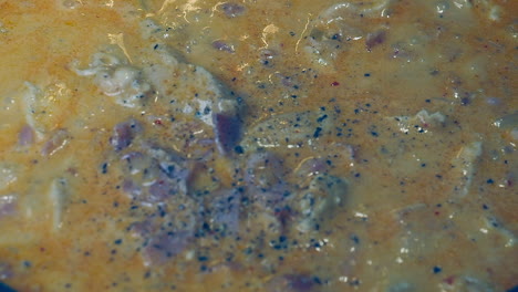 full frame close-up: black pepper is added to simmering meaty stew