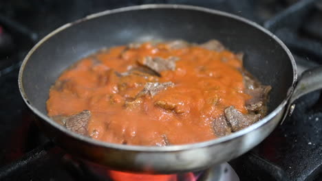 añadiendo la salsa de tomate a las tiras de ternera salteadas en una cacerola sobre la estufa de gas, preparación de kebab turco