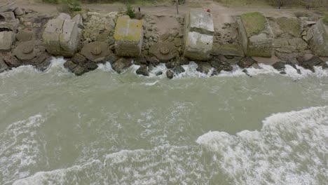 aerial birdseye view of abandoned seaside fortification buildings at karosta northern forts, baltic sea coast , large waves, overcast day, slow motion, drone dolly shot moving right