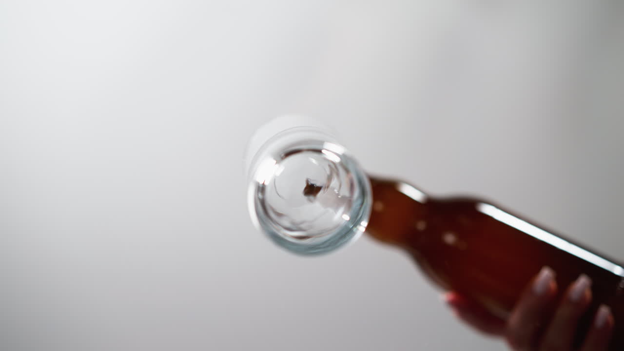 macro disparo de líquido transparente girando en una botella de vidrio sostenida por una mano femenina contra un fondo gris