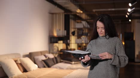 a pretty woman with dark hair looks through a catalog in a furniture store a pretty woman with dark hair looks through a catalog in a furniture store high quality footage