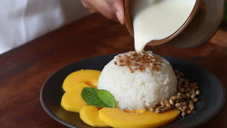 pouring coconut milk on mango sticky rice dessert