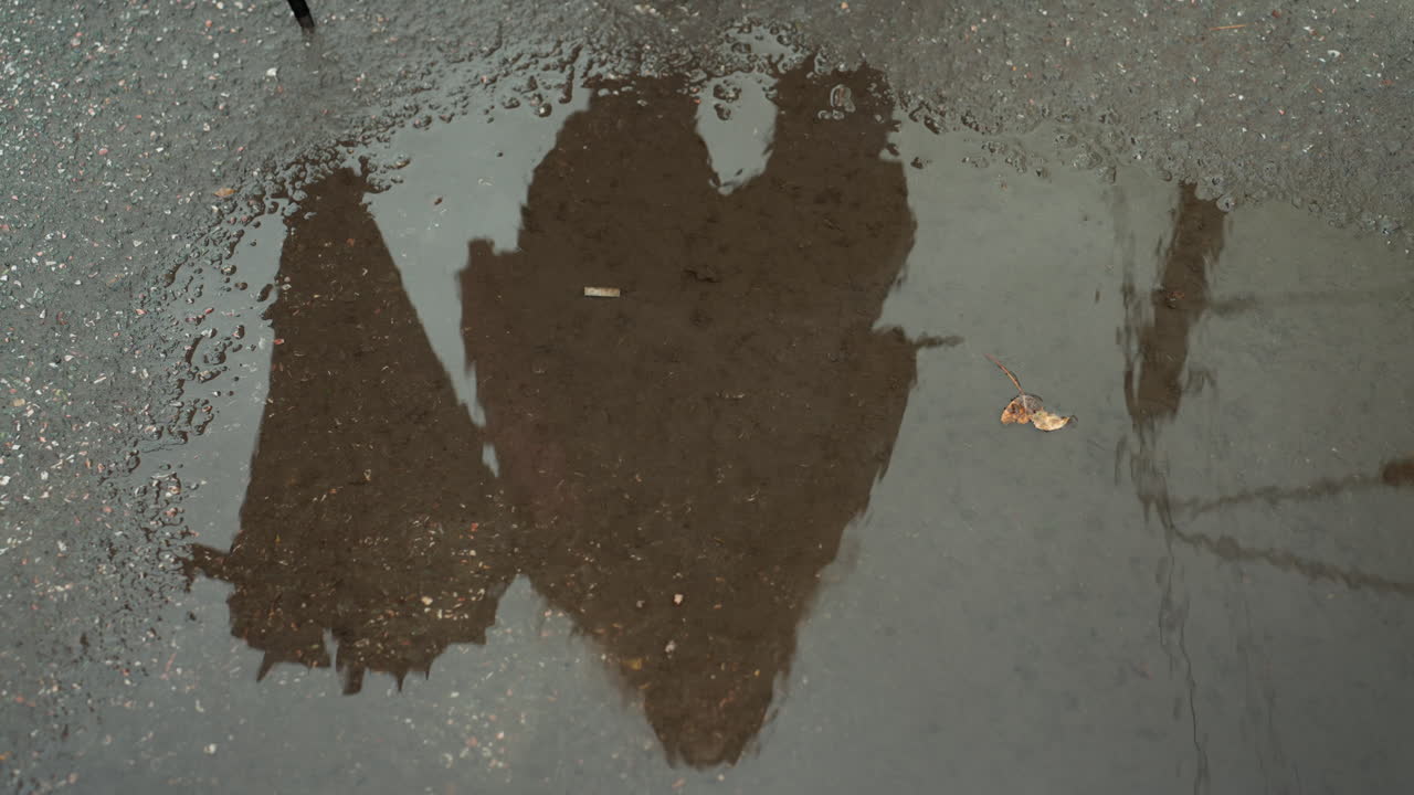 Riflesso di una passeggiata silenziosa in una notte piovosa. Silhouette pedonale silenziosa riflessa in una pozzanghera sotto un cielo nuvoloso. Scena di marciapiede deserto che raffigura un viaggiatore solitario riflesso nell'acqua con foglie autunnali