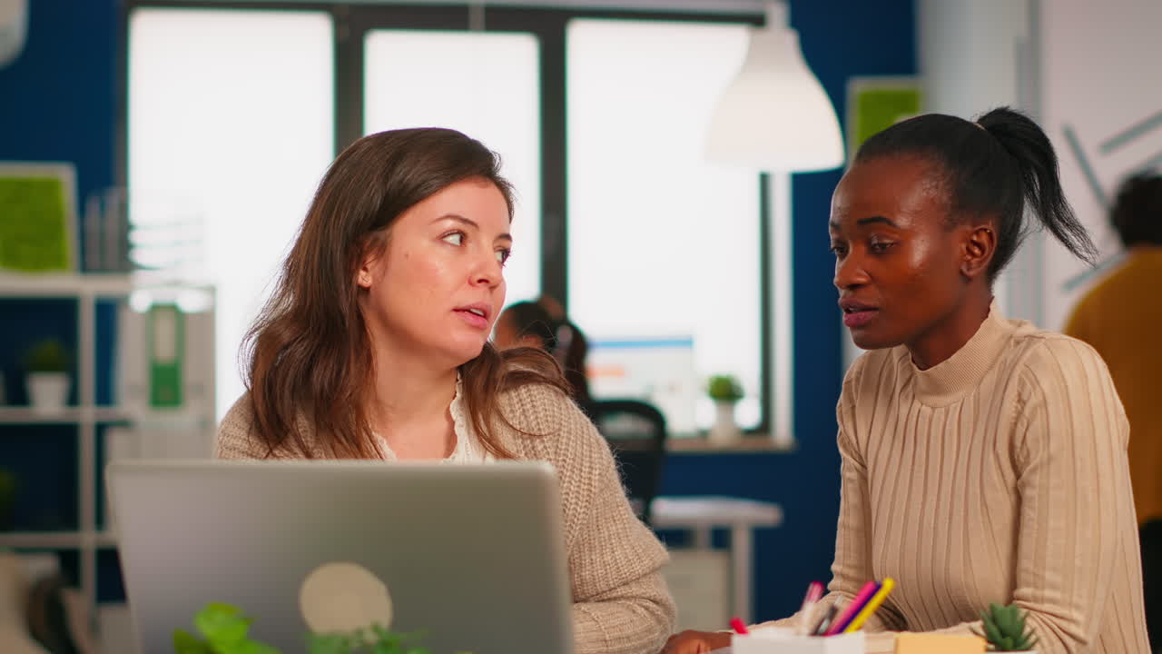 Young diverse corporate staff sitting at table in coworking office using laptop
