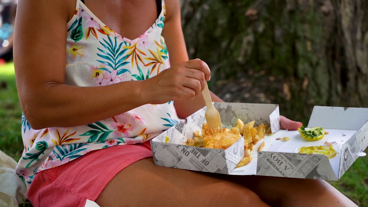 Donna che mangia fish and chips da una scatola in un parco in Inghilterra, Gloucestershire