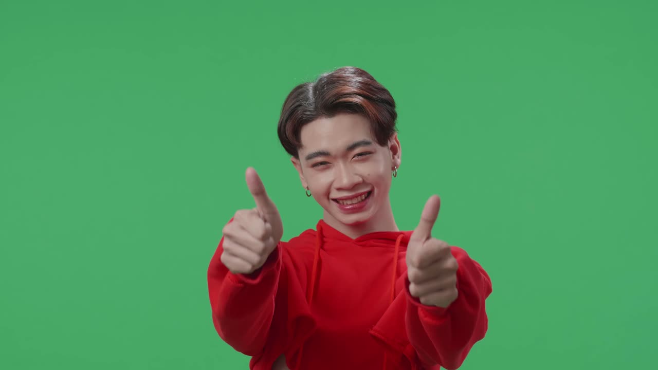Happy Asian Transgender Male Showing Thumbs Up Gesture While Standing In The Green Screen Studio