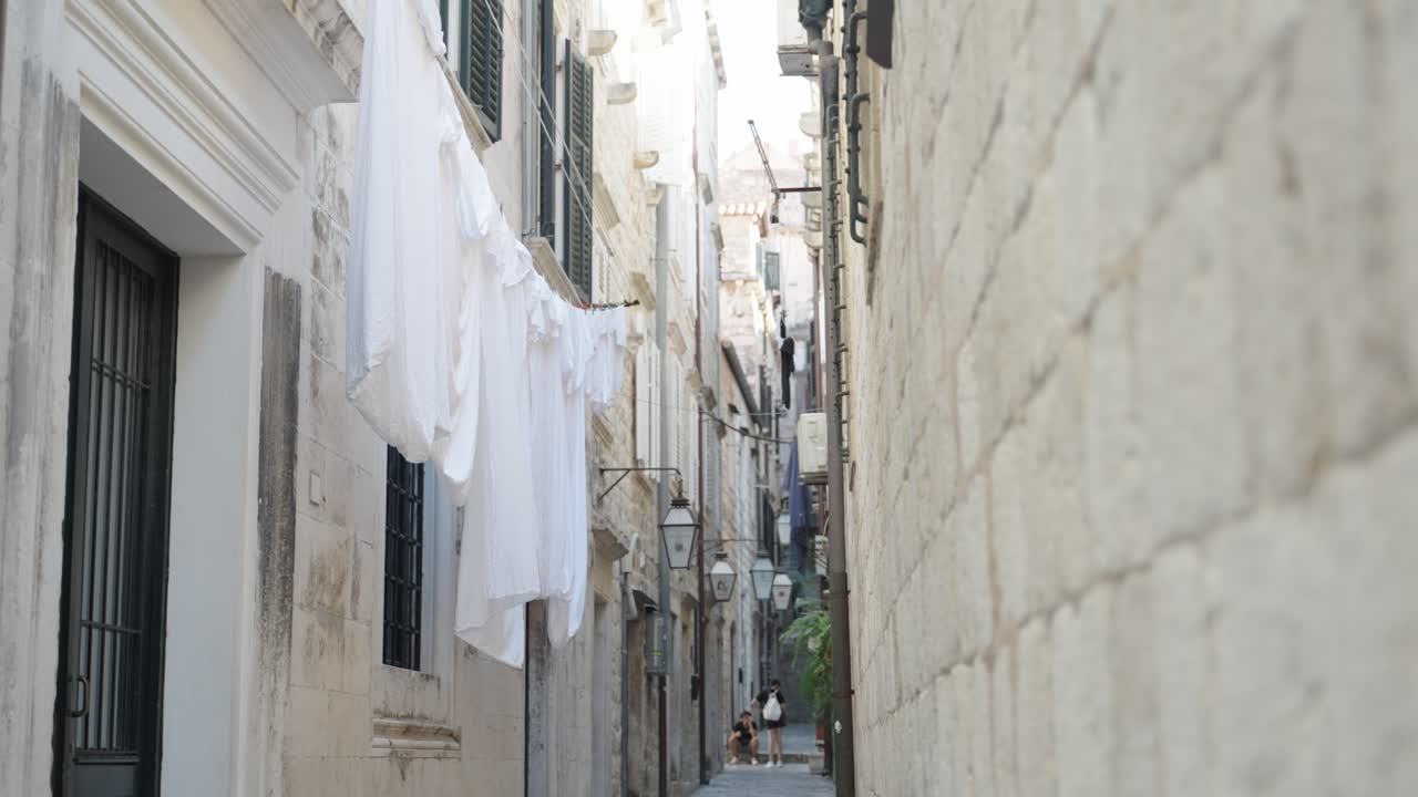 Hanging white laundry drying on air on lines in a narrow street of traditional mediterranian houses of Old Town Dubrovnik Croatia while two young man talking in the background