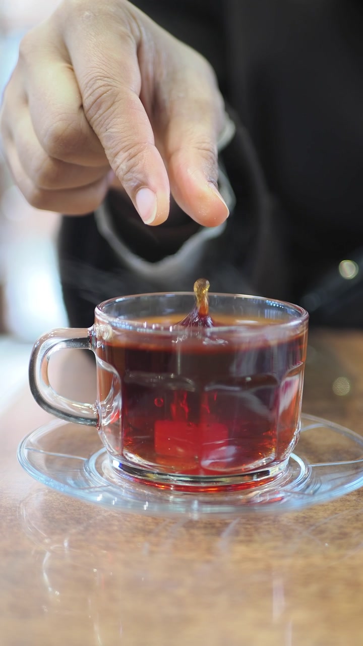 Hand Dropping Sugar Cube into Hot Tea in Glass Cup