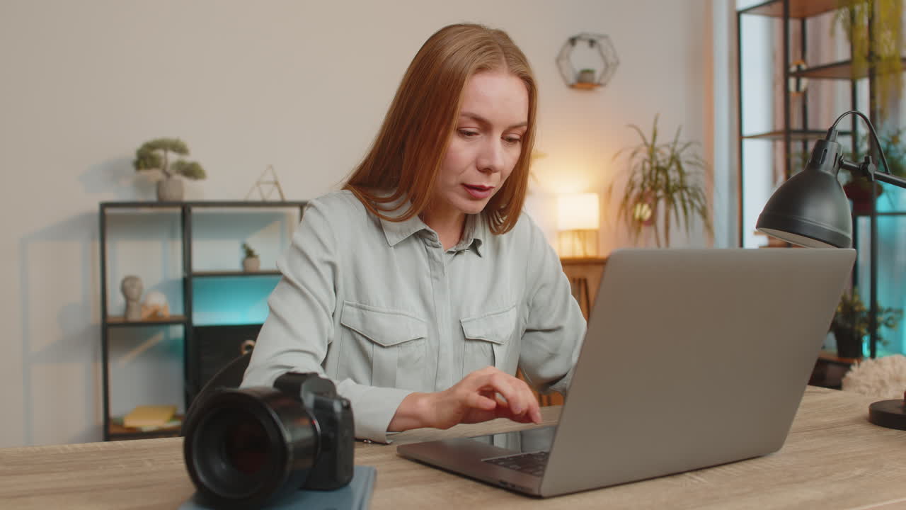Mature caucasian woman photographer transfer files from camera to laptop at home office table desk