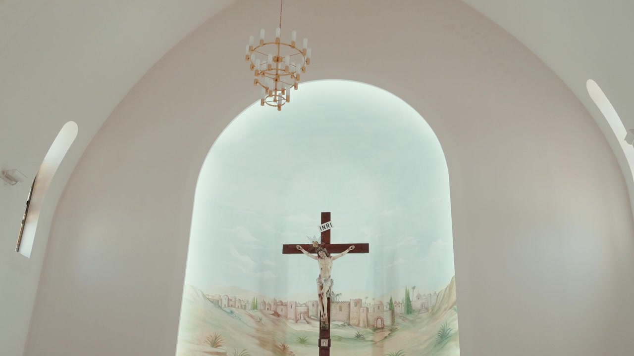 Crucifijo en un mural pintado de Jerusalén bajo un candelabro dentro de un ábside de iglesia abovedado
