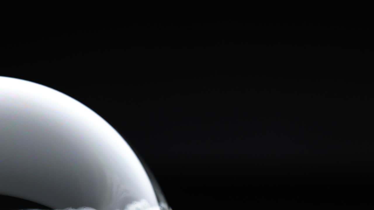 A soap bubble's surface transitions through vibrant color reflections against a dark background, highlighting light interaction and fluid dynamics