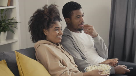 young couple laughing while watching a film on tv