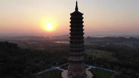 drone aerial view in vietnam flying around a buddhist pagoda in a ninh binh temple at sunset with green landscape in the horizon