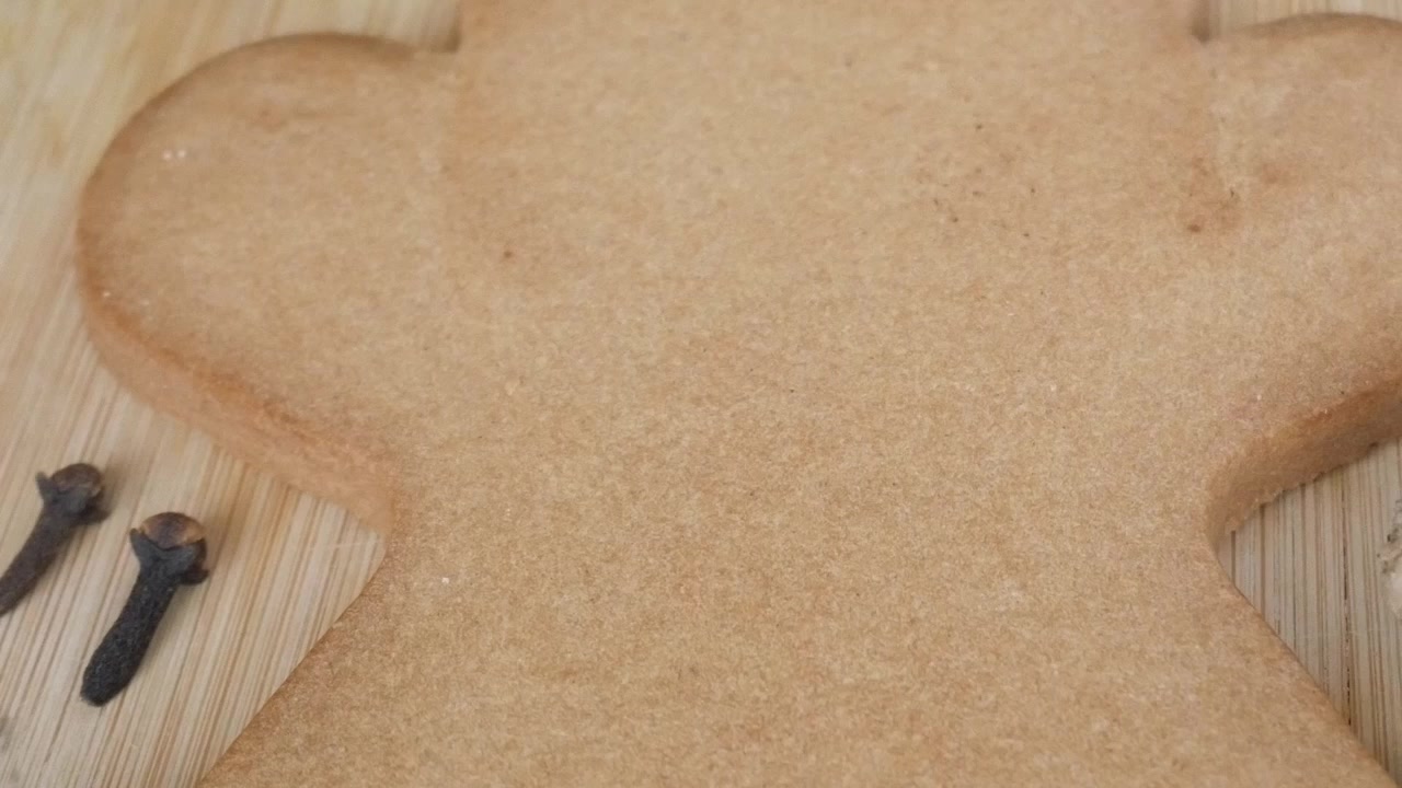 Primo piano di un grande biscotto di pan di zenzero con chiodi di garofano e altri ingredienti su un tagliere di legno