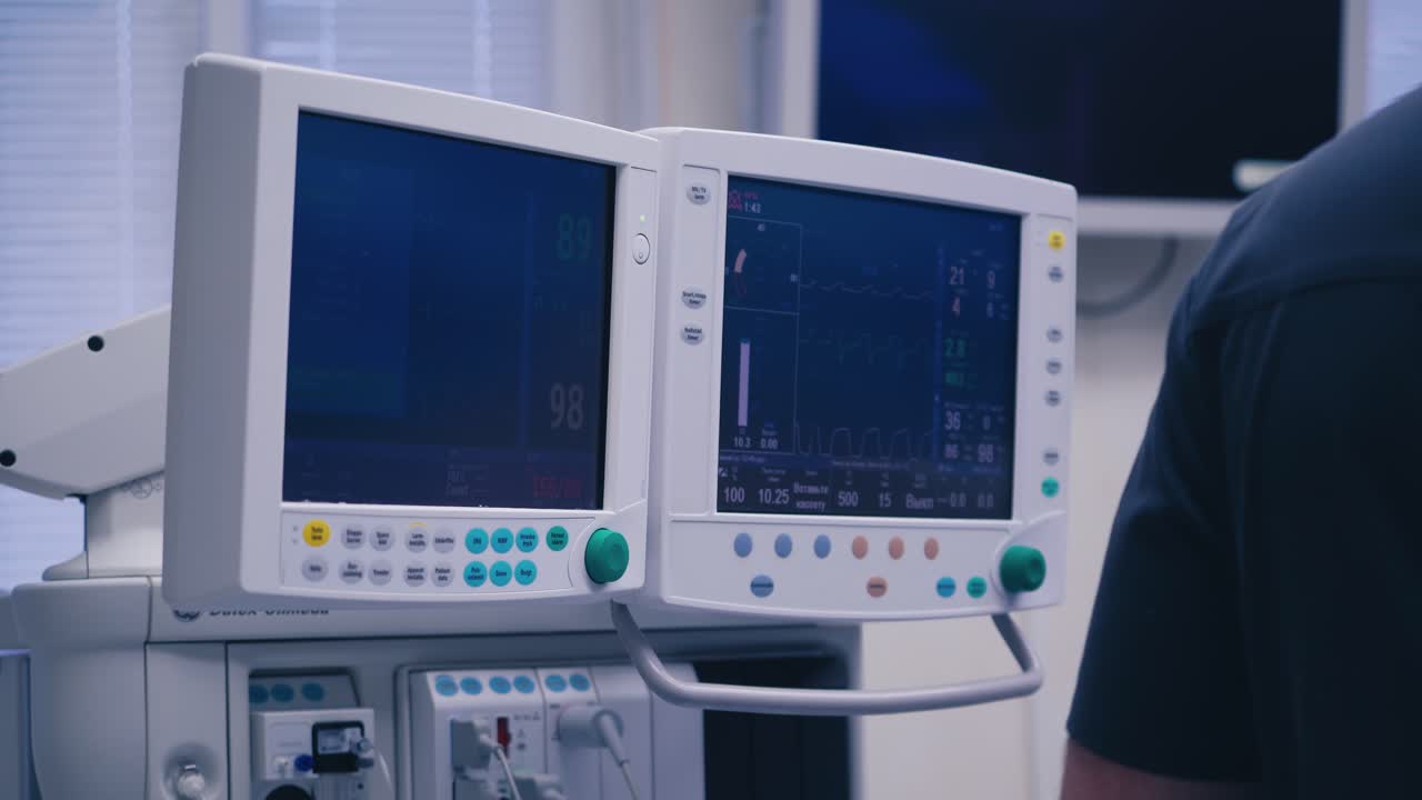 Hi-tech medical equipment. Two screens display of vital signs and cardiogram in modern clinic. Doctor is standing near monitors.