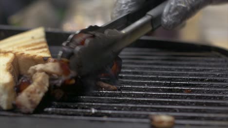 Pieces-of-pork-meat-being-tossed-on-grill-and-grilled-toast-being-removed-from-grill,-filmed-as-close-up-shot-in-handheld-style