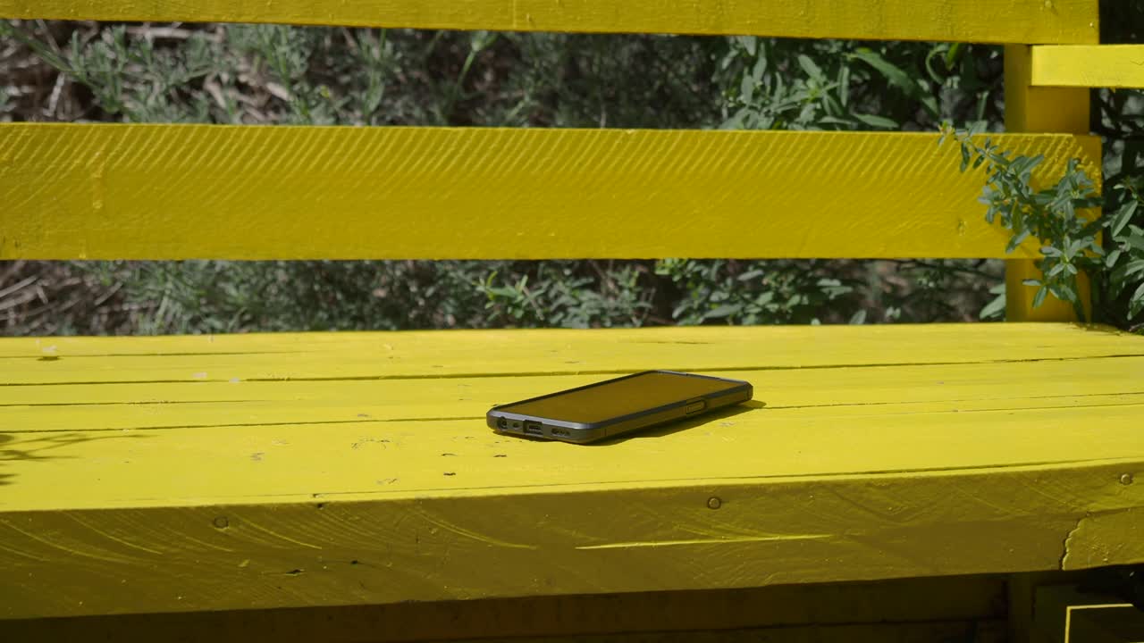 黄色い公園のベンチに置かれた携帯電話