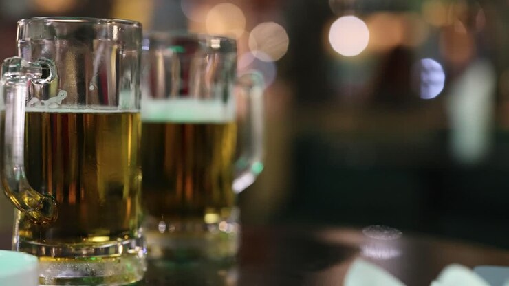 Primo piano di bicchieri di birra su un tavolo con uno sfondo sfocato e suggestivo, che crea un'atmosfera calda e accogliente.