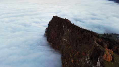 aerial flyover over the cliffs of burgenstock in luzern, switzerland as the peak is surrounded by a sea of clouds during an autumn sunset in the swiss alps