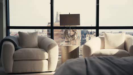 a-sitting-area-in-the-primary-bedroom-of-a-home-with-white-chairs-and-an-elegant-lamp